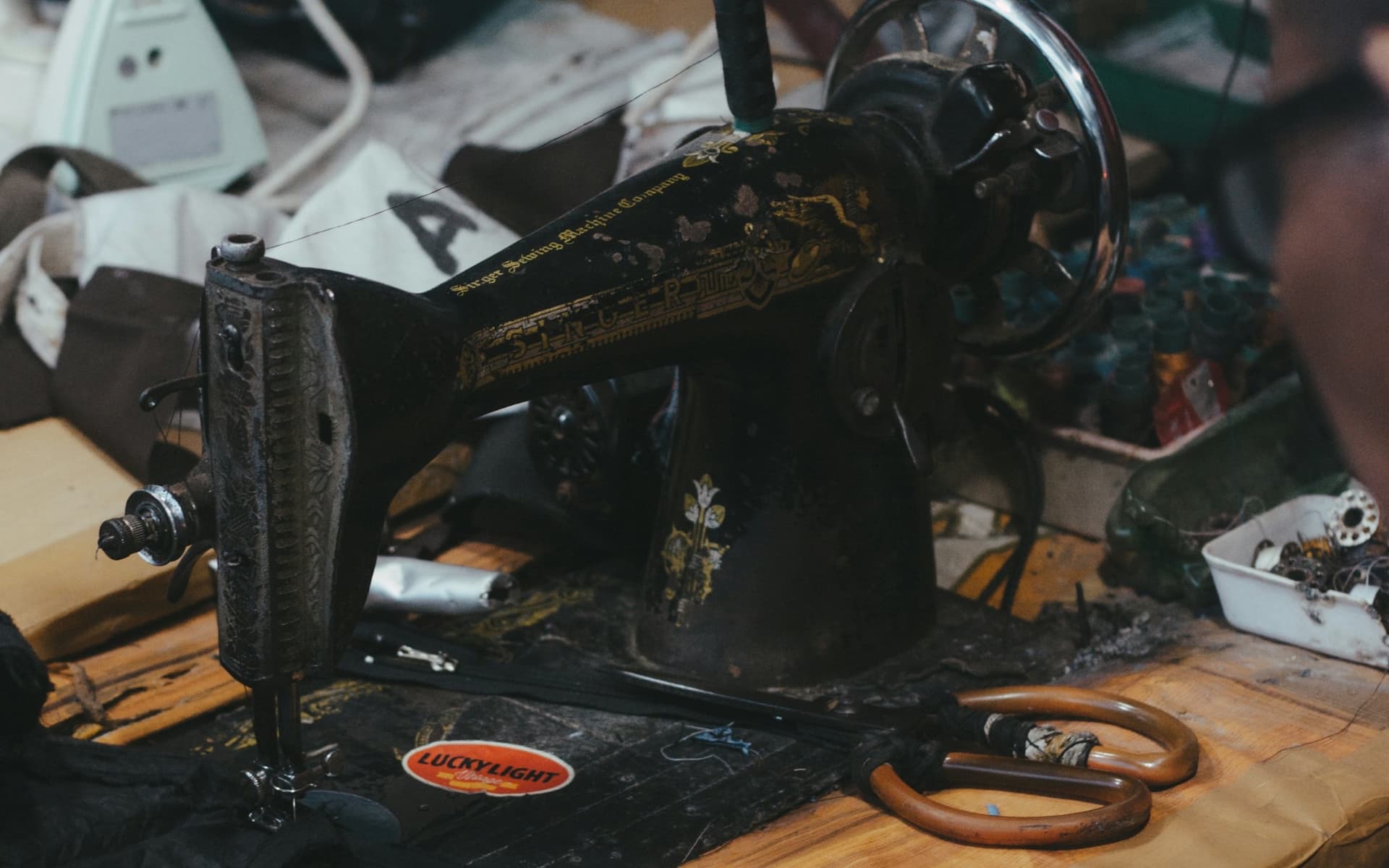 A tailor’s workbench: an old Singer sewing machine, shears and dark cloth, in a working shop.
